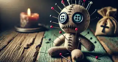 Voodoo bábika so gombíkovými očami a vyšitými ústami, prepichnutá niekoľkými špendlíkmi, sedí na starom drevenom stole v tlmenom osvetlení.